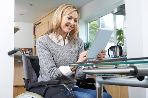 Jonge vrouw in een rolstoel die een tablet gebruikt